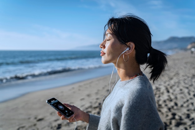 Mujer joven escuchando música en un teléfono inteligente en la playa usando auriculares