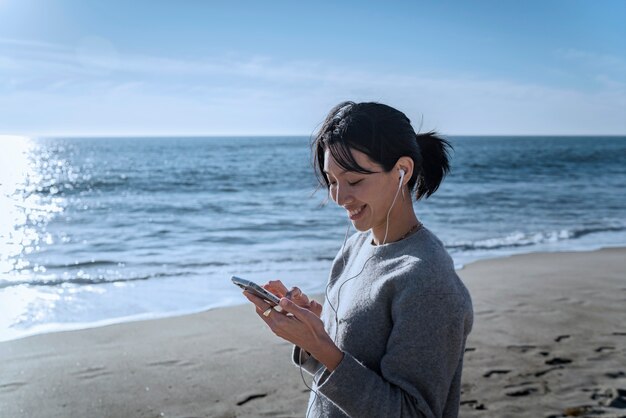 Mujer joven escuchando música en un teléfono inteligente en la playa usando auriculares