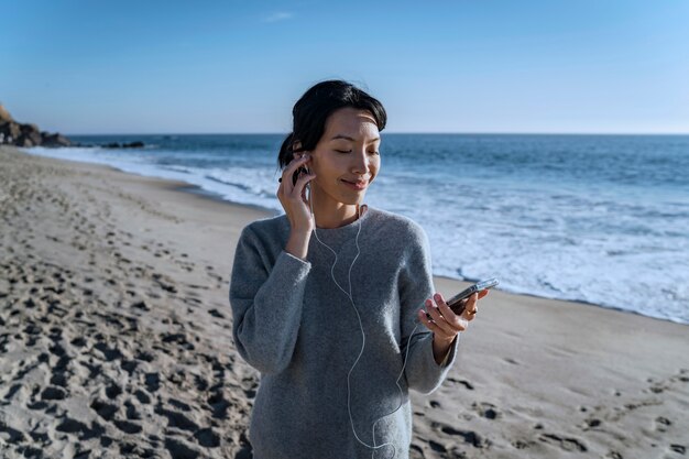 Mujer joven escuchando música en un teléfono inteligente en la playa usando auriculares