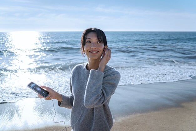 Mujer joven escuchando música en un teléfono inteligente en la playa usando auriculares