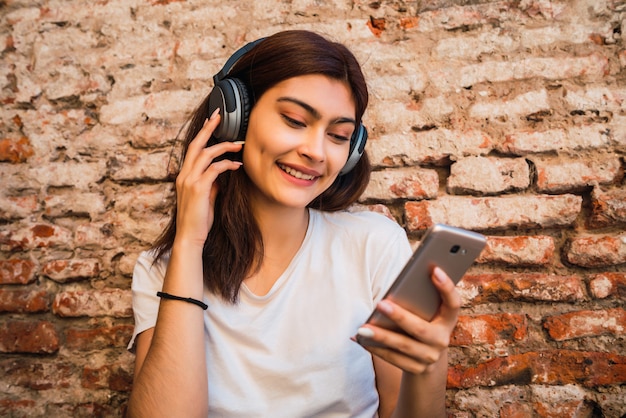 Mujer joven escuchando música y usando el teléfono inteligente.