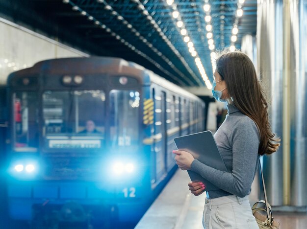 Mujer joven esperando en una estación de metro con una tableta