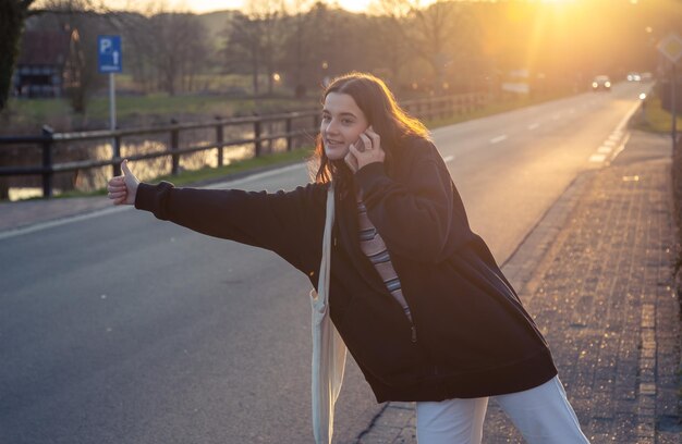 Una mujer joven esperando el transporte en automóvil al atardecer