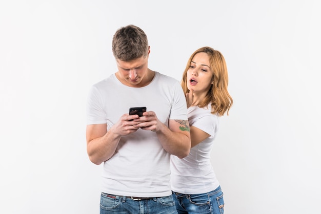 Mujer joven espiando el teléfono de su novio contra el fondo blanco