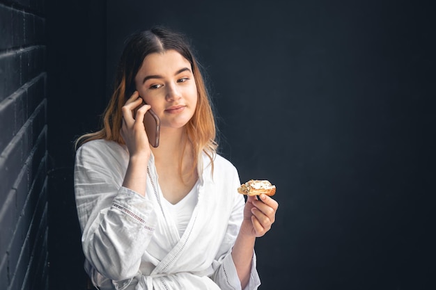 Una mujer joven está hablando por teléfono y comiendo un eclair.