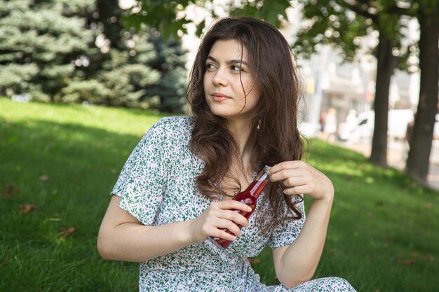 Una mujer joven está hablando en un teléfono inteligente mientras está sentada en el césped del parque