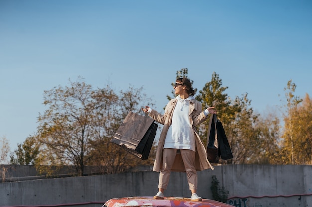 Una mujer joven está de pie en un automóvil con bolsas en las manos