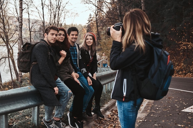 Mujer joven está tomando una foto de sus amigos en una cámara digital en el bosque de otoño.