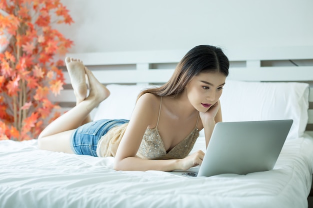 Una mujer joven está viendo una película de una computadora portátil en la cama en su casa