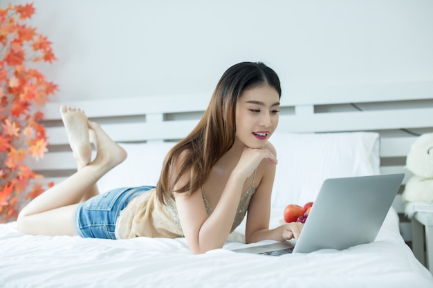 Una mujer joven está viendo una película de una computadora portátil en la cama en su casa