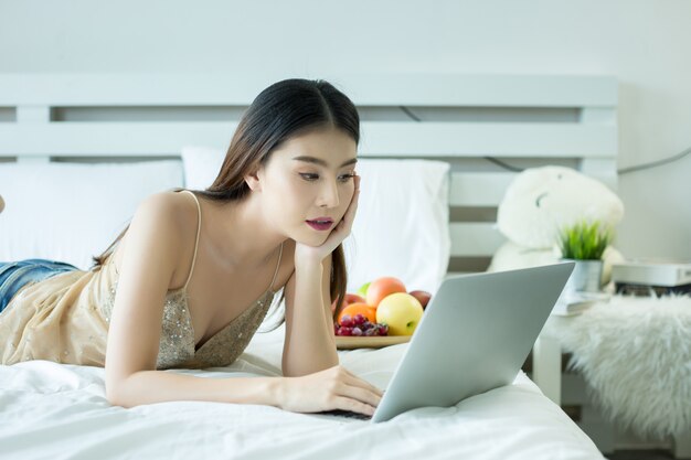 Una mujer joven está viendo una película de una computadora portátil en la cama en su casa