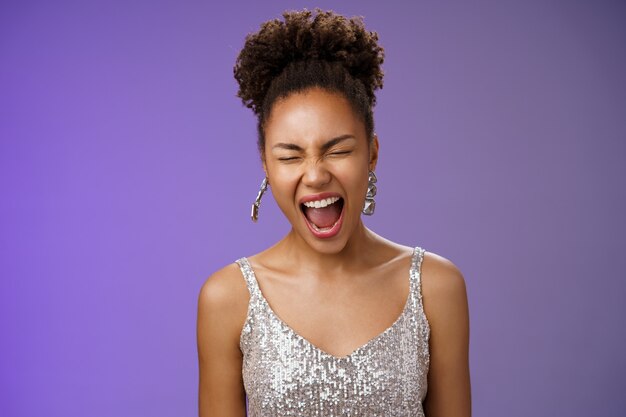 Mujer joven con estilo afroamericana de buen aspecto alegre en vestido de noche plateado ojos cerrados bostezo soñoliento partido cansado toda la noche de pie divertido fondo azul quiero dormir. Copia espacio