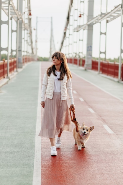 Mujer joven con estilo caminando con perro corgi al aire libre.