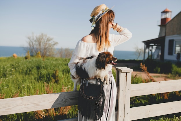 Mujer joven con estilo en el campo, sosteniendo un perro