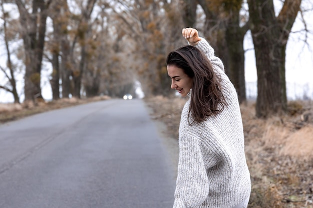 Foto gratuita mujer joven con estilo por la carretera de asfalto en la estación fría