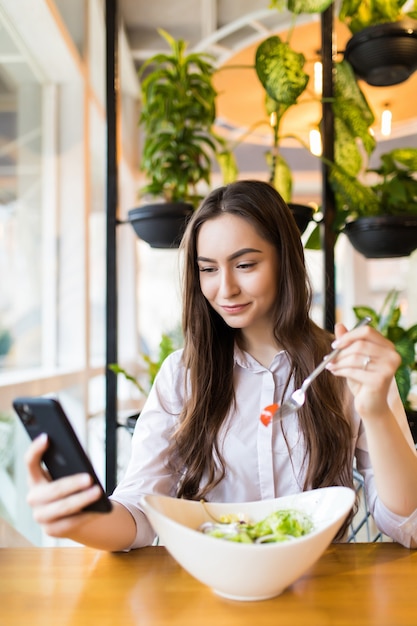 Mujer joven con estilo comiendo ensalada saludable en la terraza de un restaurante, sintiéndose feliz en un día de verano