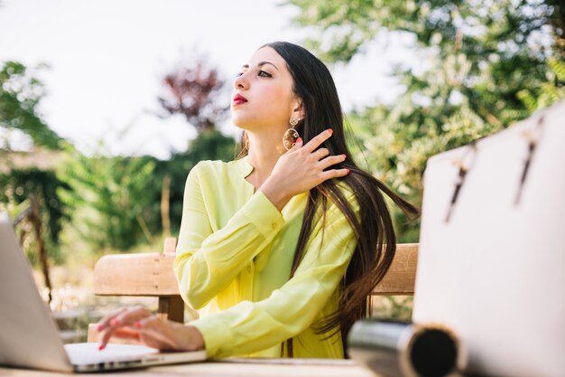 Mujer joven con estilo con la computadora portátil en el parque