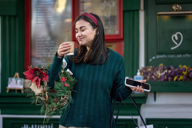 Mujer joven con estilo disfrutando de un café después de las compras navideñas.