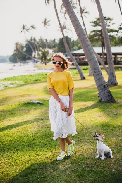 Mujer joven con estilo hipster sosteniendo caminar y jugar con perro en el baech