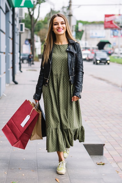 Mujer joven con estilo que camina con los bolsos de compras coloridos en la calle