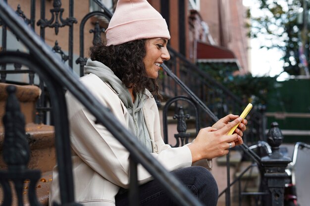 Mujer joven con estilo con smartphone mientras está sentado en las estepas de la ciudad