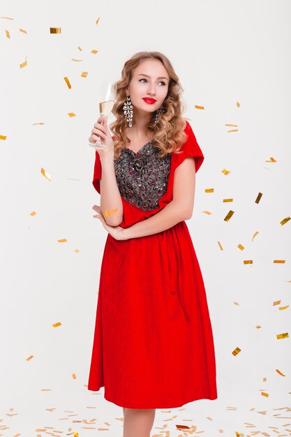 Mujer joven con estilo en vestido de noche rojo celebrando el año nuevo, sosteniendo una copa de champán