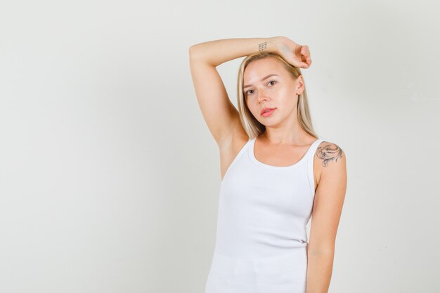 Mujer joven estirando el brazo alrededor de la cabeza en camiseta blanca