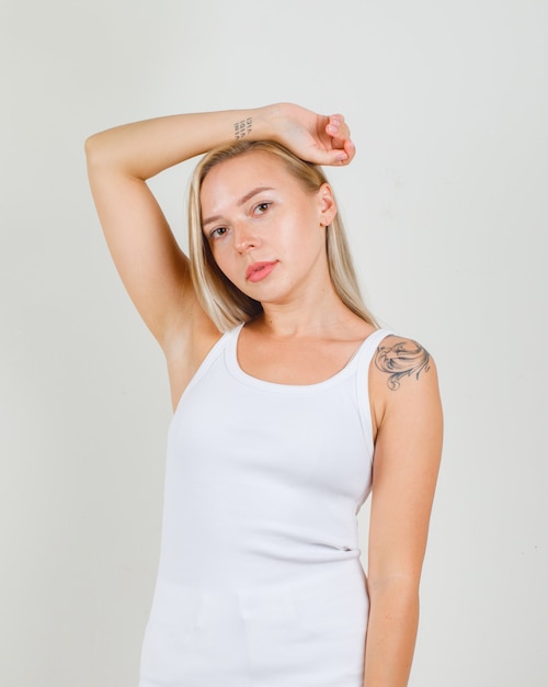 Foto gratuita mujer joven estirando el brazo alrededor de la cabeza en camiseta blanca