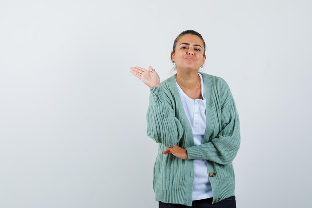 Mujer joven estirando la mano como saludo en camisa blanca y chaqueta de punto verde menta y mirando feliz