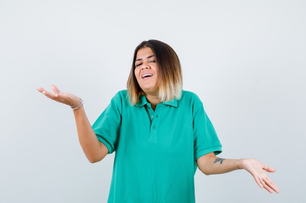 Mujer joven estirando las manos en forma de cuestionamiento en camiseta de polo y mirando dichoso. vista frontal.