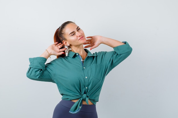 Mujer joven estirando la parte superior del cuerpo en camisa verde y mirando relajado, vista frontal.