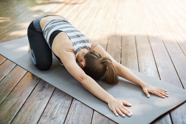 Mujer joven estirando su espalda después de una larga sesión de yoga. Haciendo ejercicios en su patio trasero para que los vecinos envidien.
