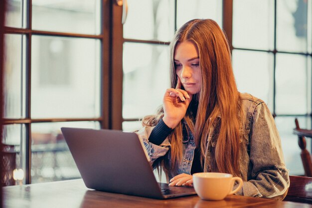 Mujer joven estudiando en la computadora portátil y tomando café en el bar