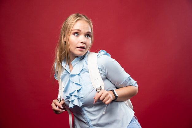 Mujer joven estudiante rubia con su mochila vuelve a la escuela y se siente encantadora y feliz.