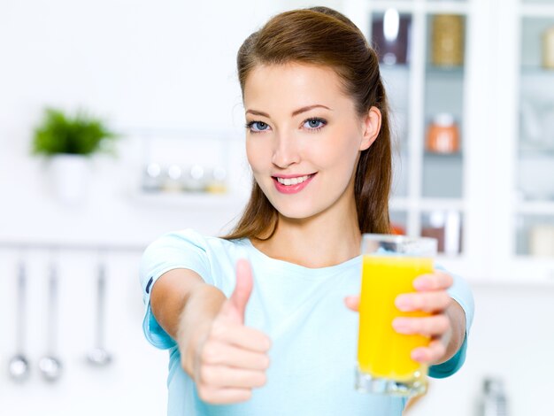 Mujer joven exitosa Thumbs-up con un vaso de jugo de naranja natural