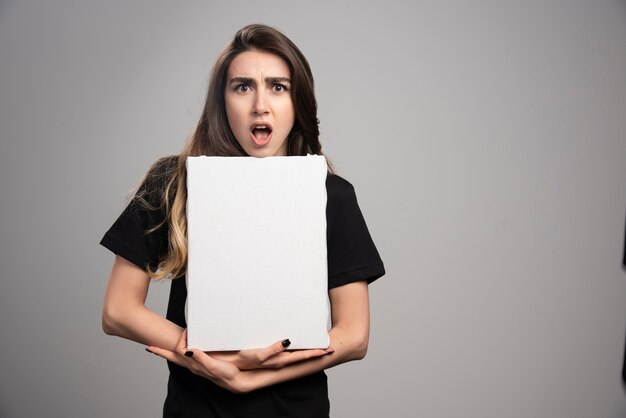 Mujer joven con expresión de asombro sosteniendo lienzo.