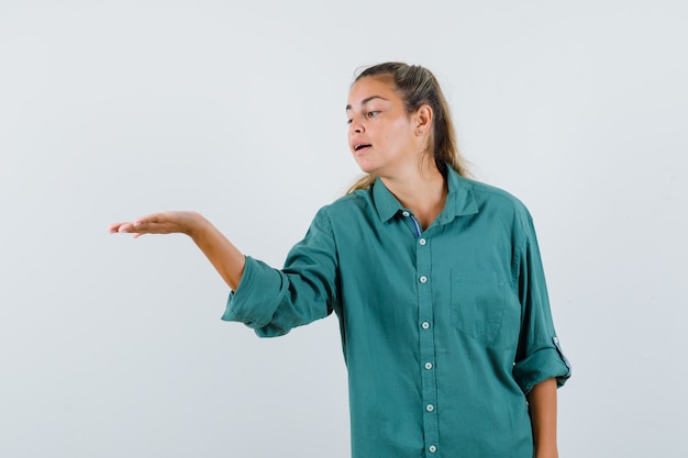 Mujer joven extendiendo la palma abierta a un lado en camisa azul y mirando concentrado