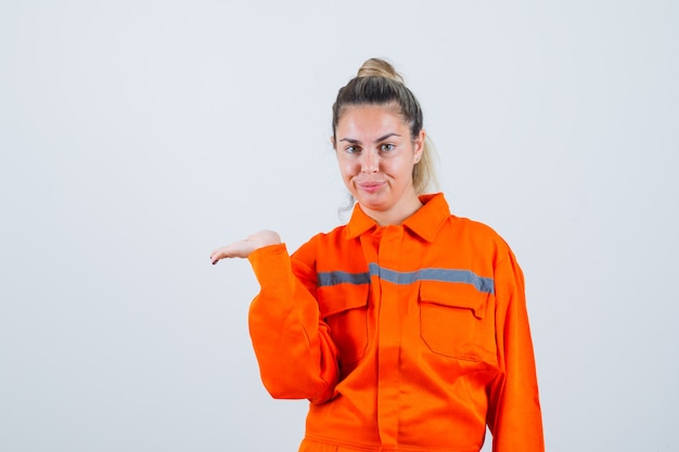 Mujer joven extendiendo la palma abierta a un lado para expresar a alguien con uniforme de trabajador y mirando atenta, vista frontal.