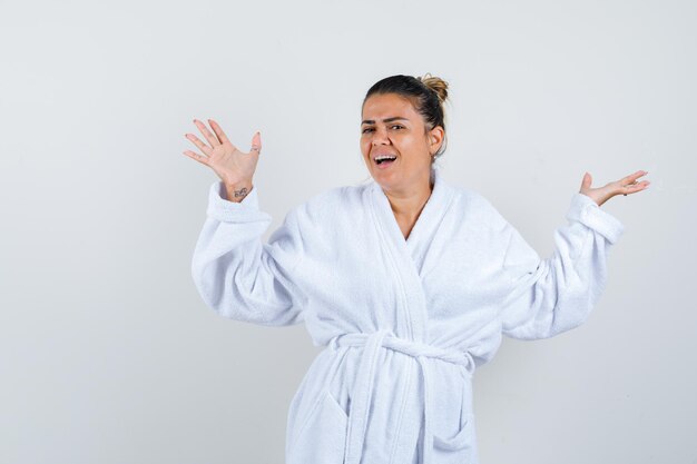 Mujer joven extendiendo las palmas a un lado en bata de baño y mirando feliz