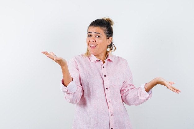 Mujer joven extendiendo las palmas a un lado en camisa rosa y mirando feliz