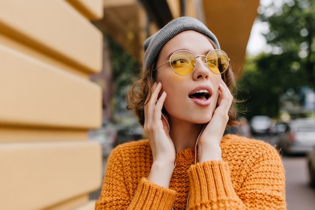 Mujer joven fascinante en gafas de sol vintage mirando a su alrededor pasar tiempo al aire libre