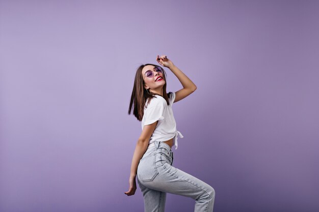 Foto gratuita mujer joven fascinante con peinado recto bailando. modelo de mujer glamorosa viste jeans y camiseta que expresa felicidad.