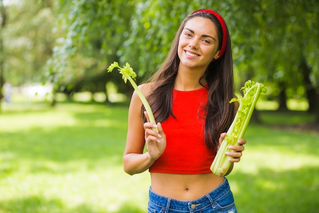 Mujer joven feliz con apio fresco en el parque