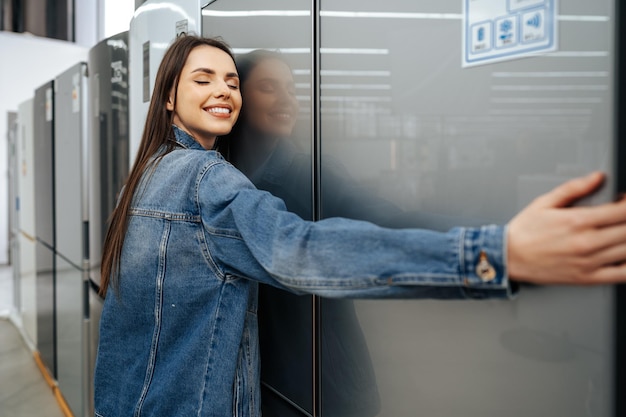 Mujer joven feliz apoyándose en su nuevo refrigerador en un centro comercial