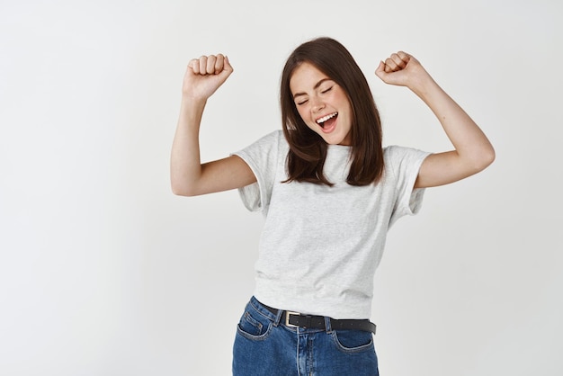 Mujer joven feliz bailando y divirtiéndose sonriendo y expresando emociones positivas de pie sobre fondo blanco.