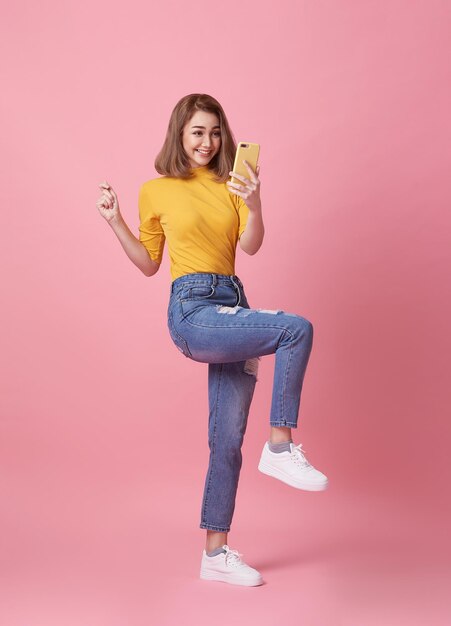 Mujer joven feliz celebrando con teléfono móvil aislado sobre fondo de color rosa