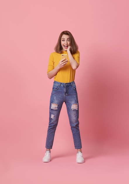 Mujer joven feliz celebrando con teléfono móvil aislado sobre fondo rosa.