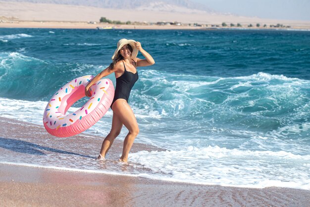 Una mujer joven feliz con un círculo de natación en forma de rosquilla junto al mar. El concepto de ocio y entretenimiento en vacaciones.