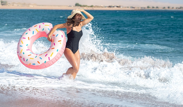 Una mujer joven feliz con un círculo de natación en forma de rosquilla junto al mar. El concepto de ocio y entretenimiento en vacaciones.