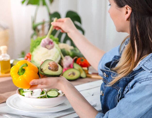 Mujer joven y feliz comiendo ensalada en la mesa